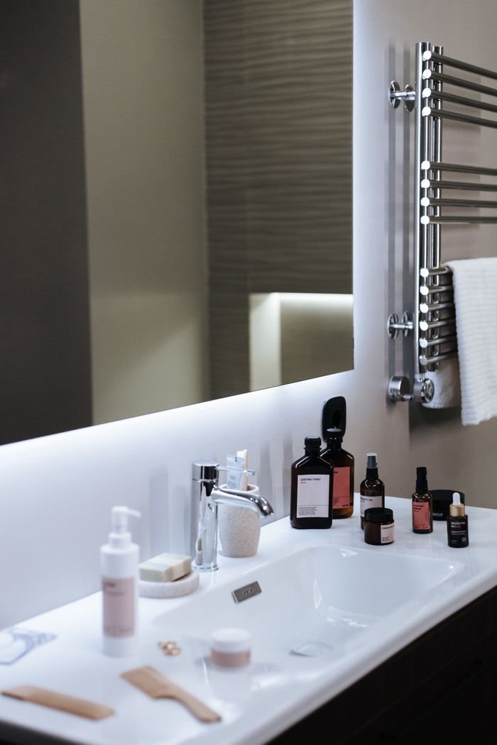 Elegant bathroom sink setup with cosmetics and mirror, offering modern aesthetic and copy space.